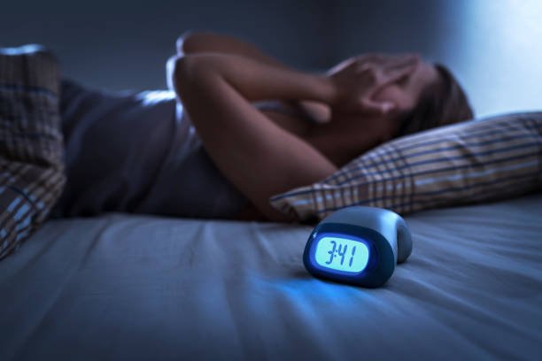 Person suffering from sleep disorder and insomnia at night with alarm clock showing 3:41 am